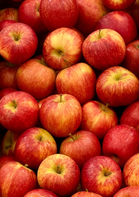 A close-up image of numerous fresh apples piled together, predominantly featuring red and yellow skin with a smooth, shiny surface. The apples are closely packed, filling the entire frame, with some showing faint streaks of green and subtle natural variations in color. The texture of the apples' skin appears firm and glossy, reflecting light, and the stems are partially visible on some, protruding slightly from the top. The background is filled with more apples, creating a dense, abundant appearance typical of a fruit display or market. The vibrant coloration and polished finish suggest they are recently harvested and ready for sale or consumption. This image is suitable for illustrating fresh produce, fruit markets, or healthy eating themes closely related to waste management by emphasizing the importance of reducing food waste and promoting proper disposal or usage of edible waste, with a subtle connection to responsible consumer habits that Waste Disposal Maida Vale might support for local households and businesses.